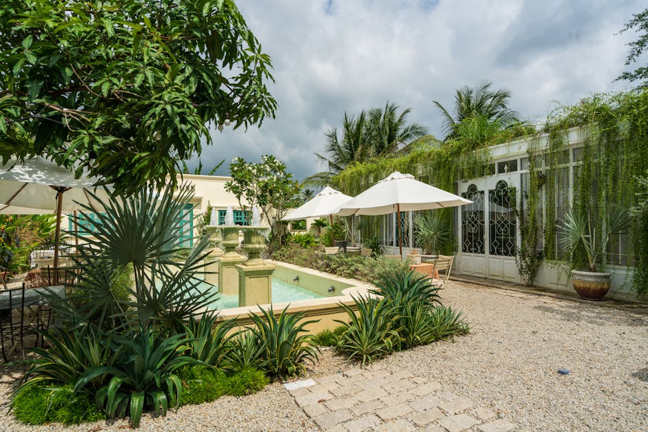 Serene courtyard featuring lush plants and an elegant fountain under a partly cloudy sky.