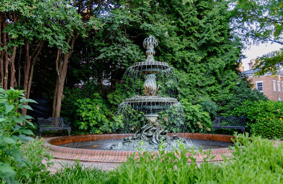 A tranquil garden with a tiered fountain surrounded by lush greenery and benches.